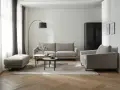 Nowoczesny salon w beżach i szarościach. Wygodna sofa, fotel i pufa na tle stonowanych kolorów.