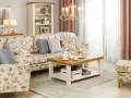 Przytulny salon w stylu shabby chic, z sofą i fotelem w kwieciste wzory, drewnianym stolikiem kawowym i kremową komodą.