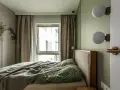 Przytulna, mała sypialnia z łóżkiem, zieloną pościelą i oknem z zasłonami. Dwie kule lamp na ścianie.