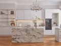 Elegancka kuchnia glamour z marmurową wyspą, białymi frontami i kryształowym żyrandolem.