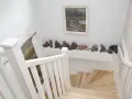 Jak wykończyć klatkę schodową w domu? Jasne drewno, białe balustrady i ciekawa ekspozycja rzeźb tworzą przytulną przestrzeń.