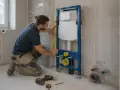 Instalator sprawdza poziomem, jak zabudować stelaż WC. Widać narzędzia i elementy instalacji.