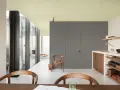 Jasny, pastelowy sufit w kolorze ścian tworzy spójną, minimalistyczną przestrzeń. Wnętrze z drewnianymi meblami i dużą ilością światła.