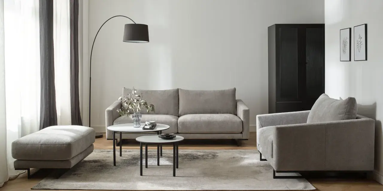 Nowoczesny salon w beżach i szarościach. Wygodna sofa, fotel i pufa na tle stonowanych kolorów.