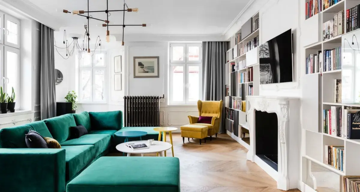 Elegancki salon w stylu francuskim z turkusową kanapą, żółtym fotelem i regałami pełnymi książek.