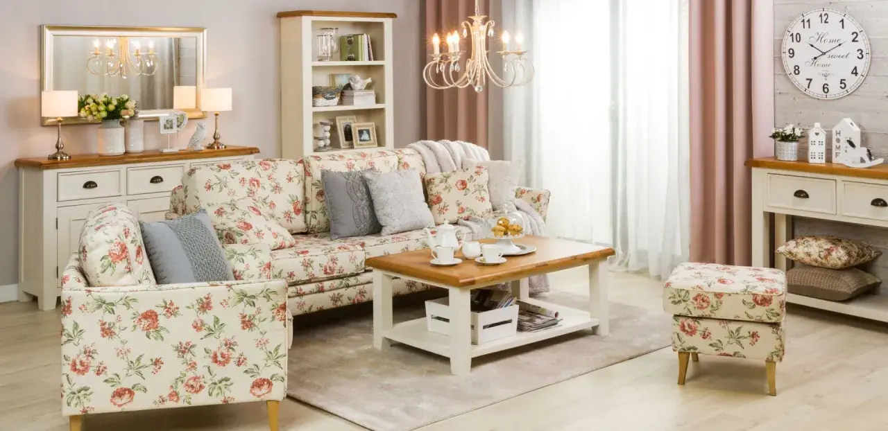 Przytulny salon w stylu shabby chic, z sofą i fotelem w kwieciste wzory, drewnianym stolikiem kawowym i kremową komodą.