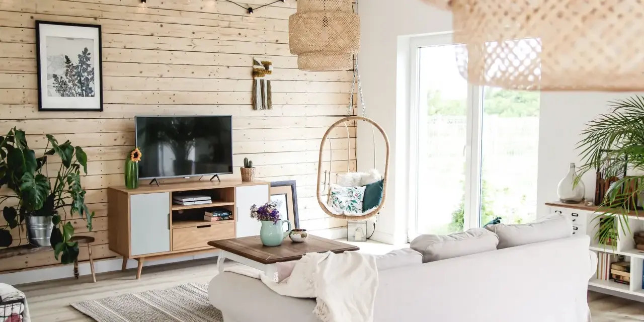 Przytulny salon z drewnianą ścianą, gdzie stara boazeria w nowej odsłonie tworzy ciepłą atmosferę. Wygodna sofa, wiszący fotel i rośliny dodają uroku.