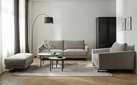 Nowoczesny salon w beżach i szarościach. Wygodna sofa, fotel i pufa na tle stonowanych kolorów.