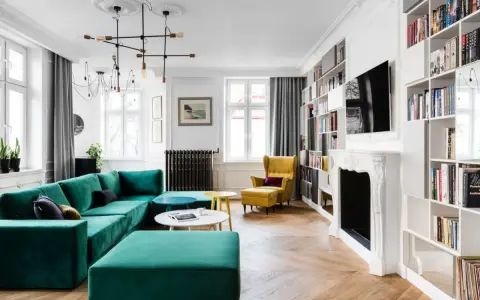 Elegancki salon w stylu francuskim z turkusową kanapą, żółtym fotelem i regałami pełnymi książek.