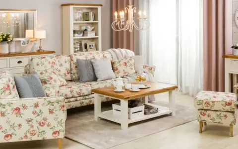Przytulny salon w stylu shabby chic, z sofą i fotelem w kwieciste wzory, drewnianym stolikiem kawowym i kremową komodą.