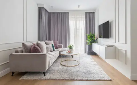 Eleganckie mieszkanie w stylu modern classic z jasną sofą, złotym stolikiem i dekoracyjnymi sztukateriami na ścianach.