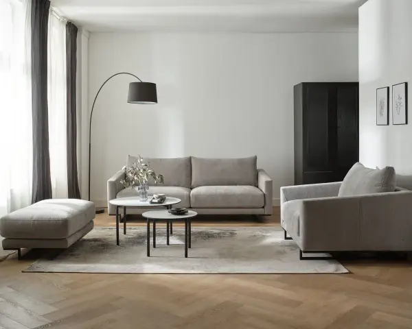 Nowoczesny salon w beżach i szarościach. Wygodna sofa, fotel i pufa na tle stonowanych kolorów.