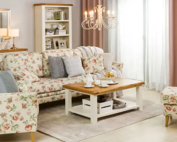 Przytulny salon w stylu shabby chic, z sofą i fotelem w kwieciste wzory, drewnianym stolikiem kawowym i kremową komodą.
