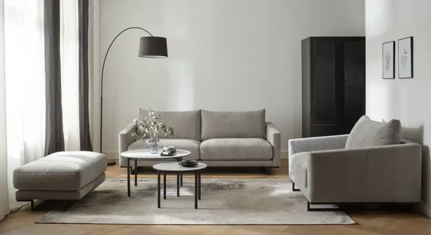 Nowoczesny salon w beżach i szarościach. Wygodna sofa, fotel i pufa na tle stonowanych kolorów.