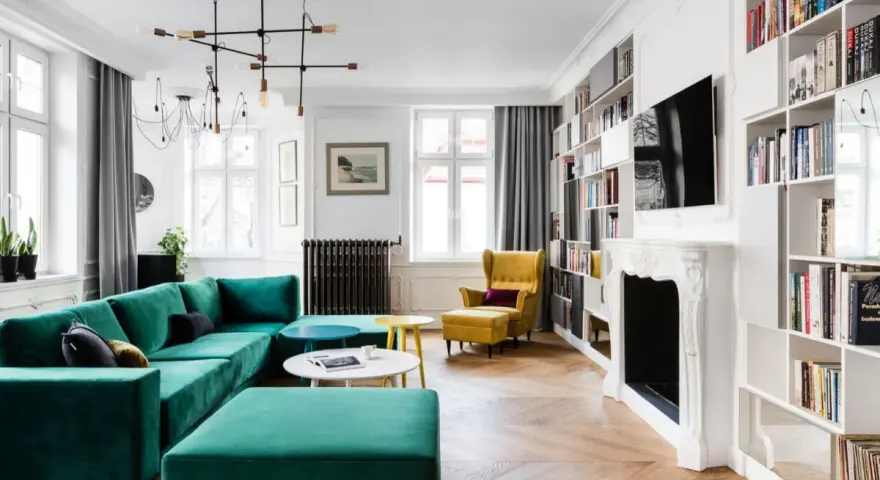 Elegancki salon w stylu francuskim z turkusową kanapą, żółtym fotelem i regałami pełnymi książek.