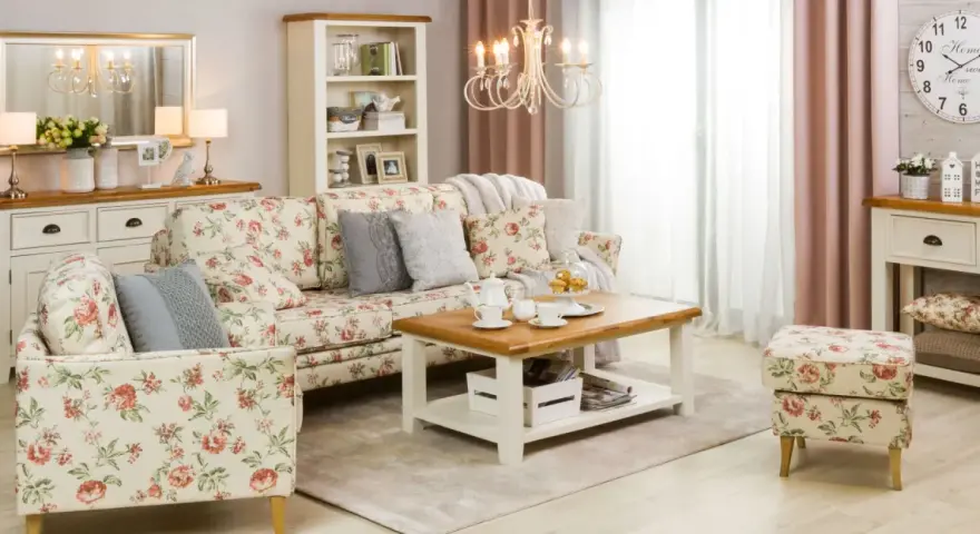 Przytulny salon w stylu shabby chic, z sofą i fotelem w kwieciste wzory, drewnianym stolikiem kawowym i kremową komodą.