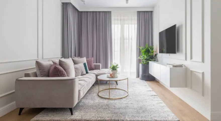 Eleganckie mieszkanie w stylu modern classic z jasną sofą, złotym stolikiem i dekoracyjnymi sztukateriami na ścianach.