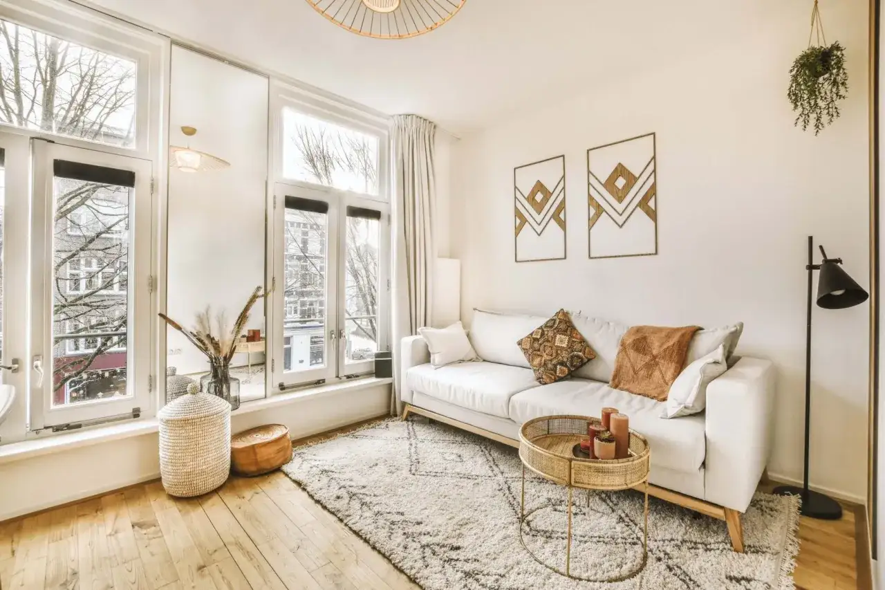 Przytulny salon w stylu scandi boho. Jasna sofa, pleciony kosz, dywan z geometrycznym wzorem i naturalne dodatki tworzą ciepłą atmosferę.